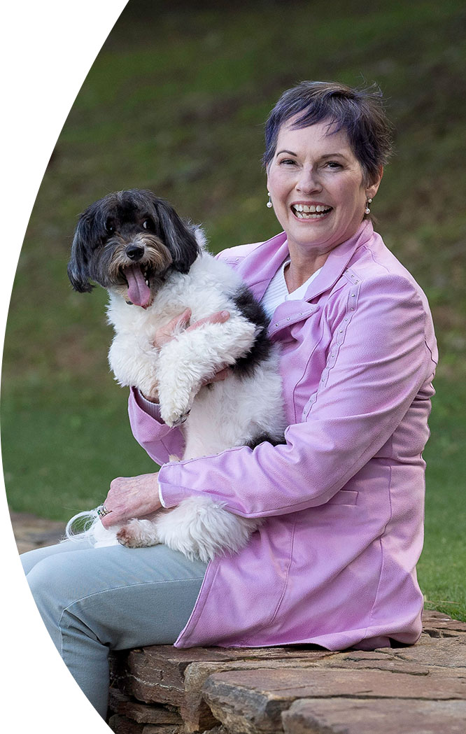 A smiling woman, sitting on a wall, holding a happy dog