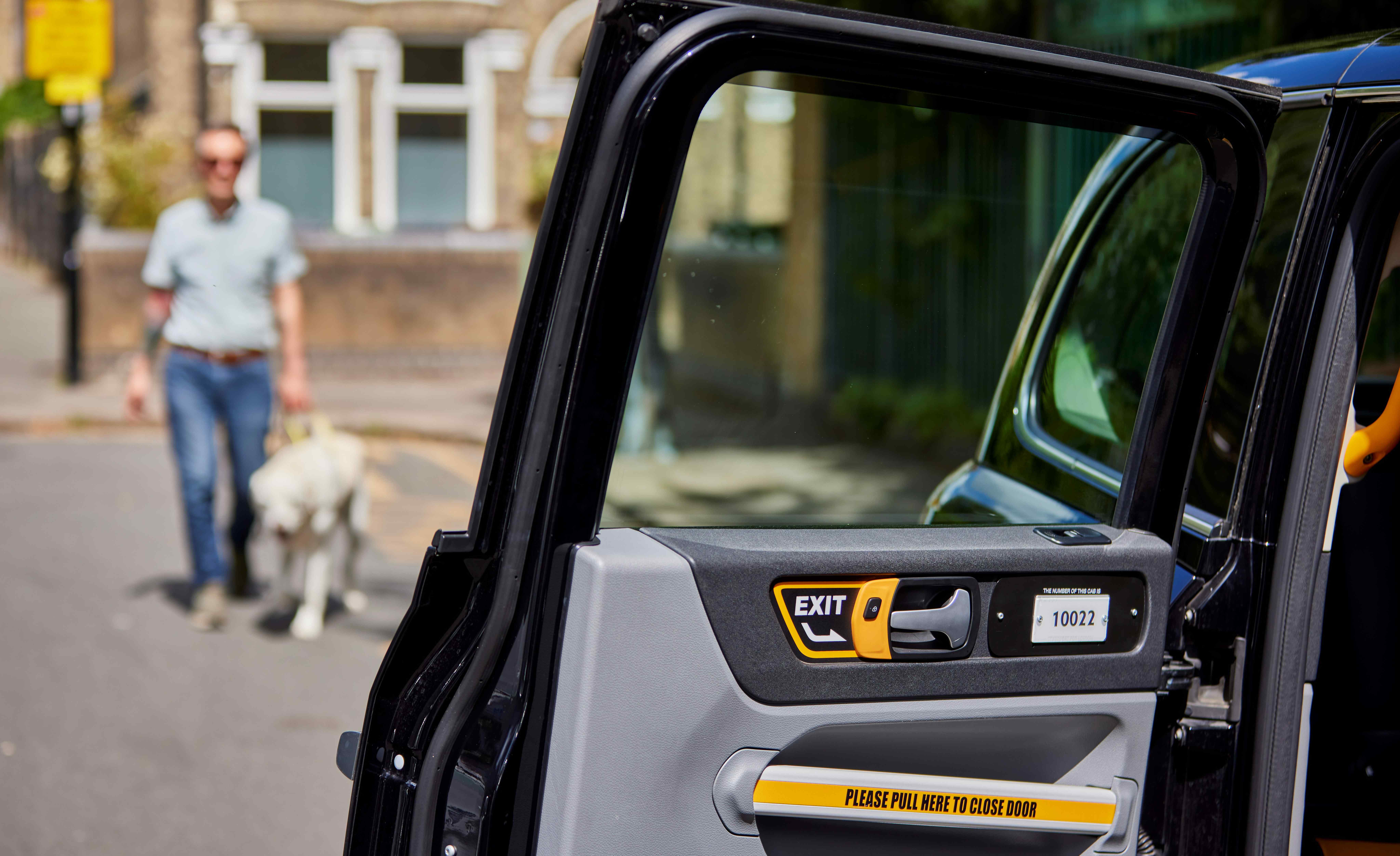 Man approaching the open door of a taxi with his guide dog, a yellow Labrador. 