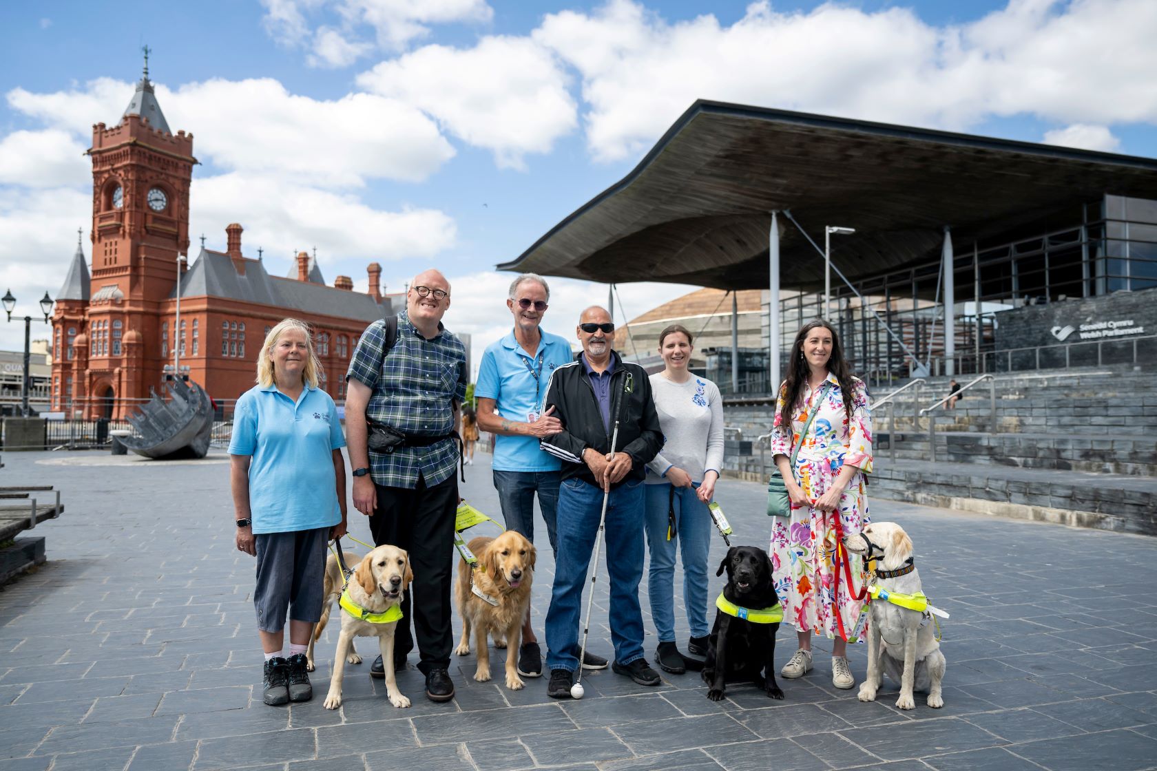 A guide dog owner waits for a bus at a floating bus stop.  A cyclist squeezes past him on the left.