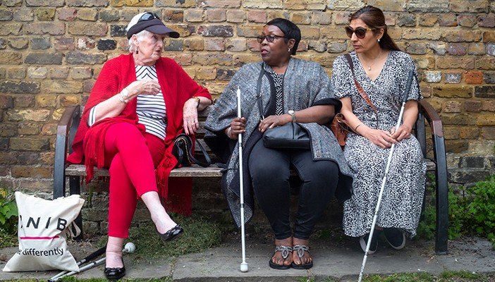 Three women talking to each other on a bench outside the RNIB office