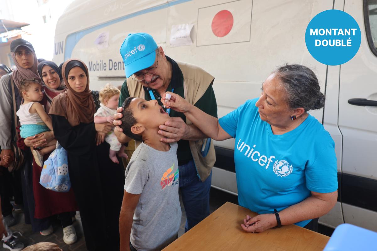 Deux vaccinateurs de l’UNICEF aident un enfant à recevoir une dose orale du vaccin contre le poliovirus, tandis que des familles font la queue en arrière-plan.