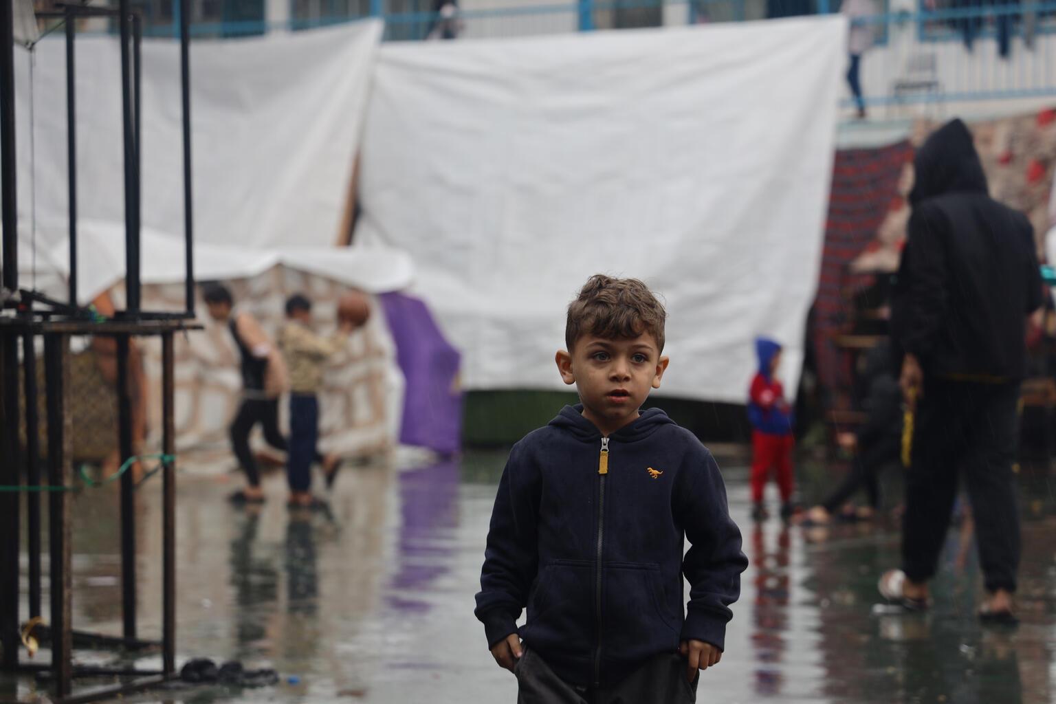 A young boy stands outside in the rain.