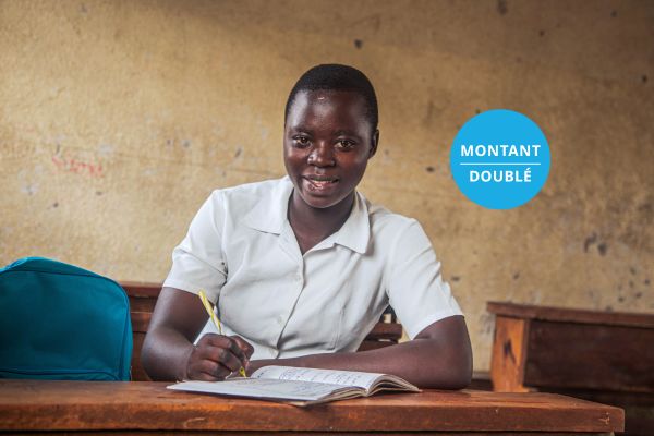 Portrait d’une élève assise à un pupitre écrivant dans un cahier et regardant l’objectif avec une expression neutre, avec le texte MONTANT DOUBLÉ en superposition.