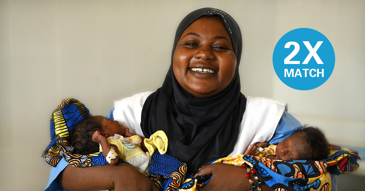A nutritionist, at the “Mère et Enfants” Health Center of Maradi, in the South of Niger holding two infants in her arms while smiling at camera.