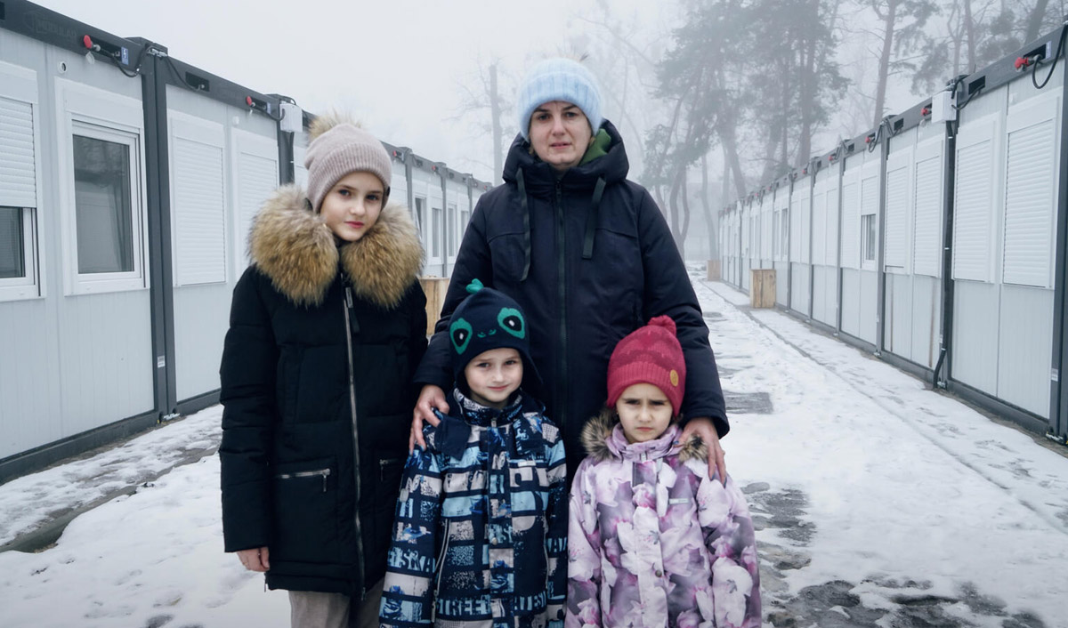 A mother and her three children wearing winter clothes stand outside in the snow. 