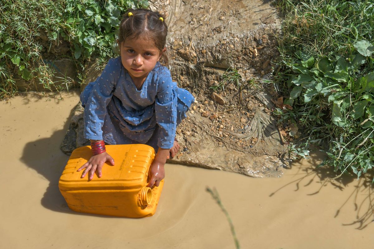 In Afghanistan, a girl collecting dirty water with a yellow water jug looks at the camera. 