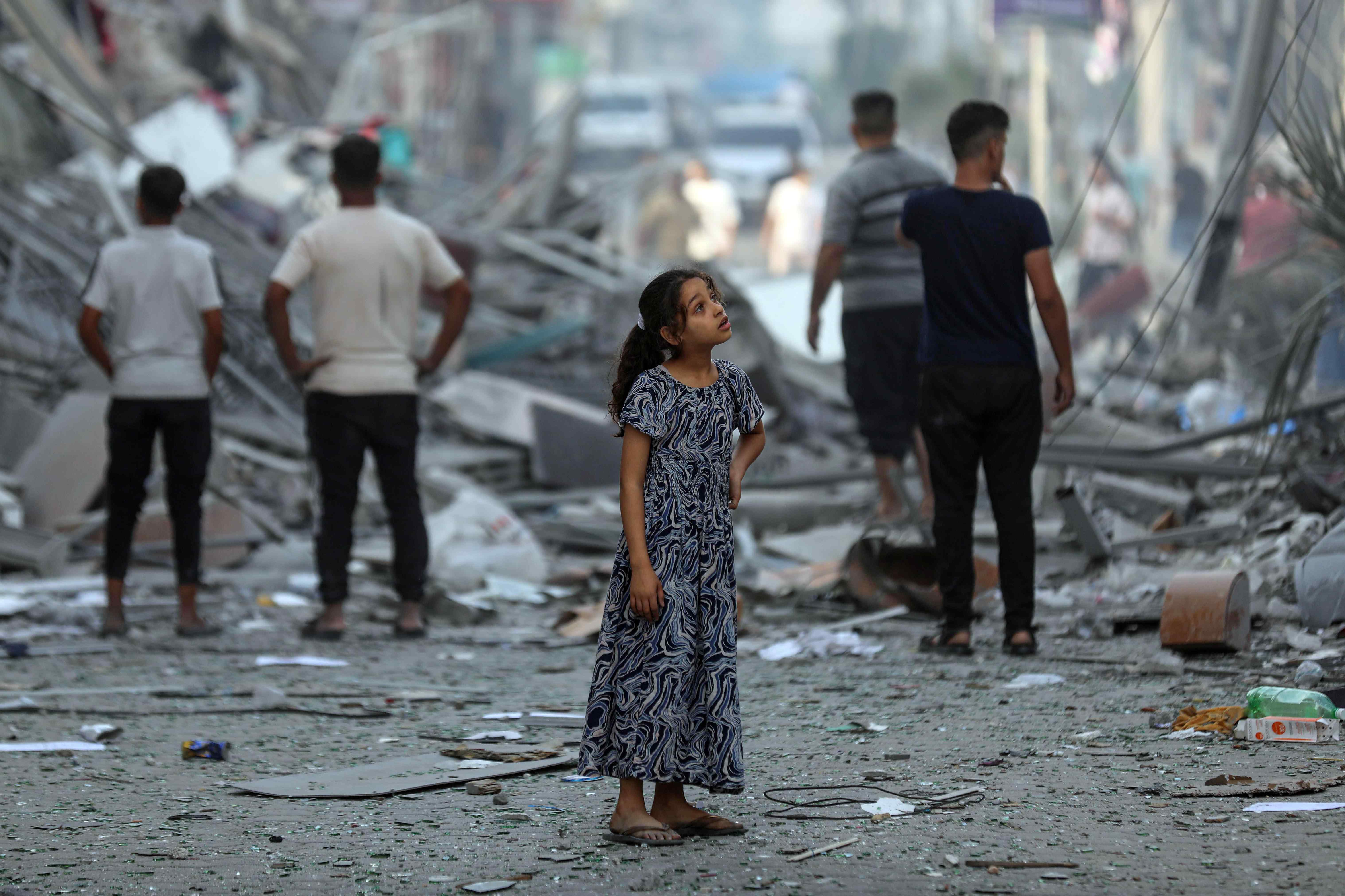 A young girl stands in the middle of a street covered in debris in Gaza.
