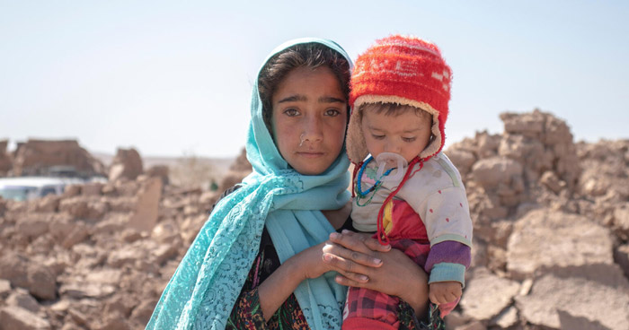 A 10-year-old girl holds her brother in front of their collapsed house in Afghanistan.