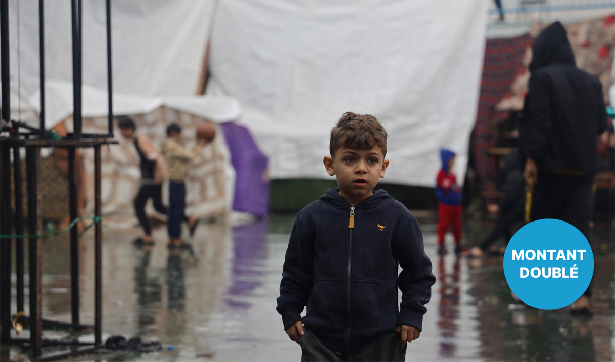 Un jeune garçon se tient dehors sous la pluie.