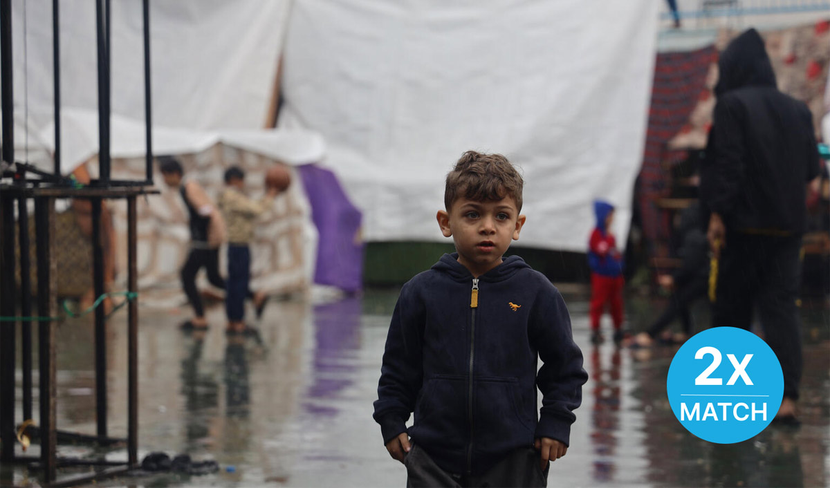 A young boy stands outside in the rain.