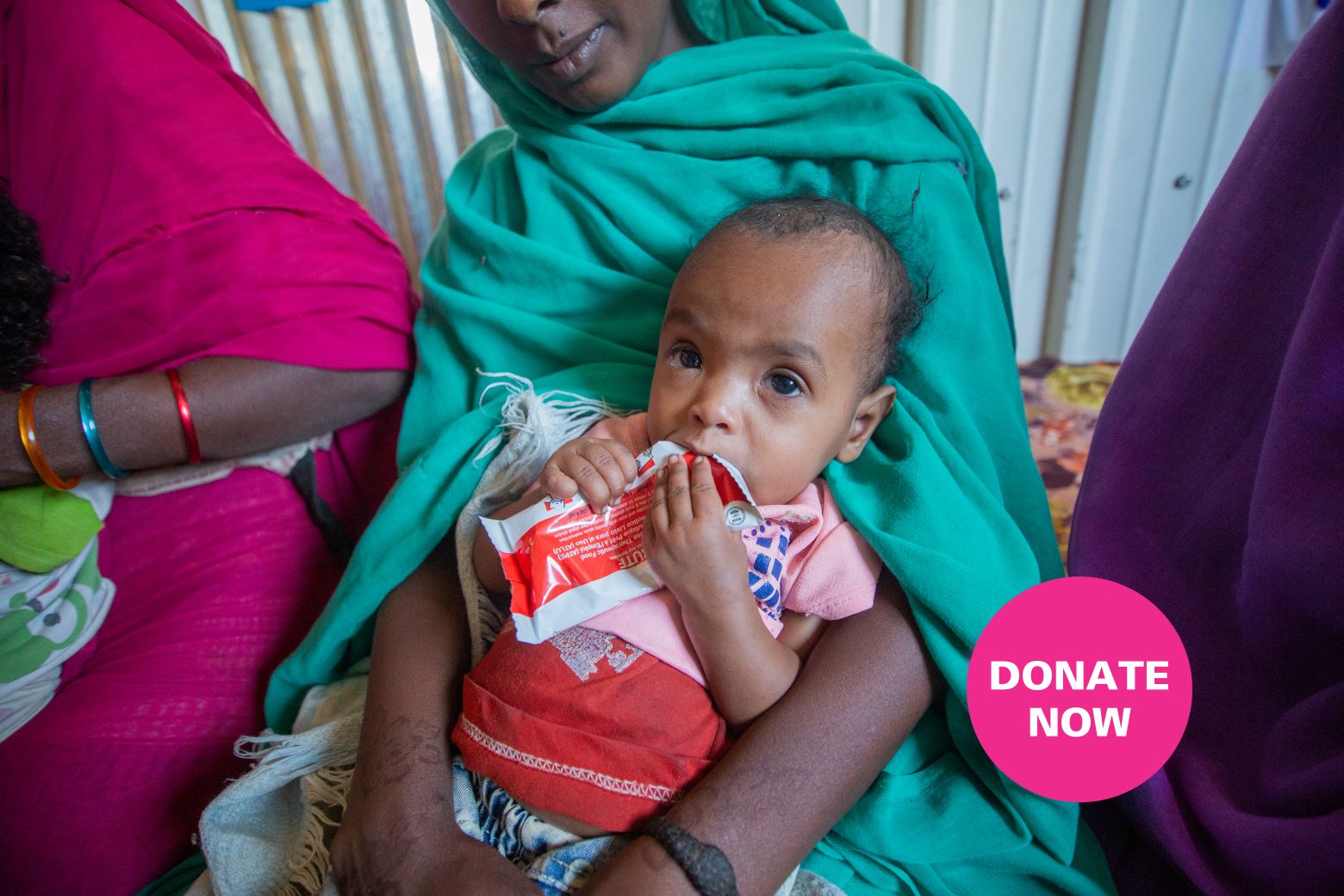 A young child eating while being held by her mother.