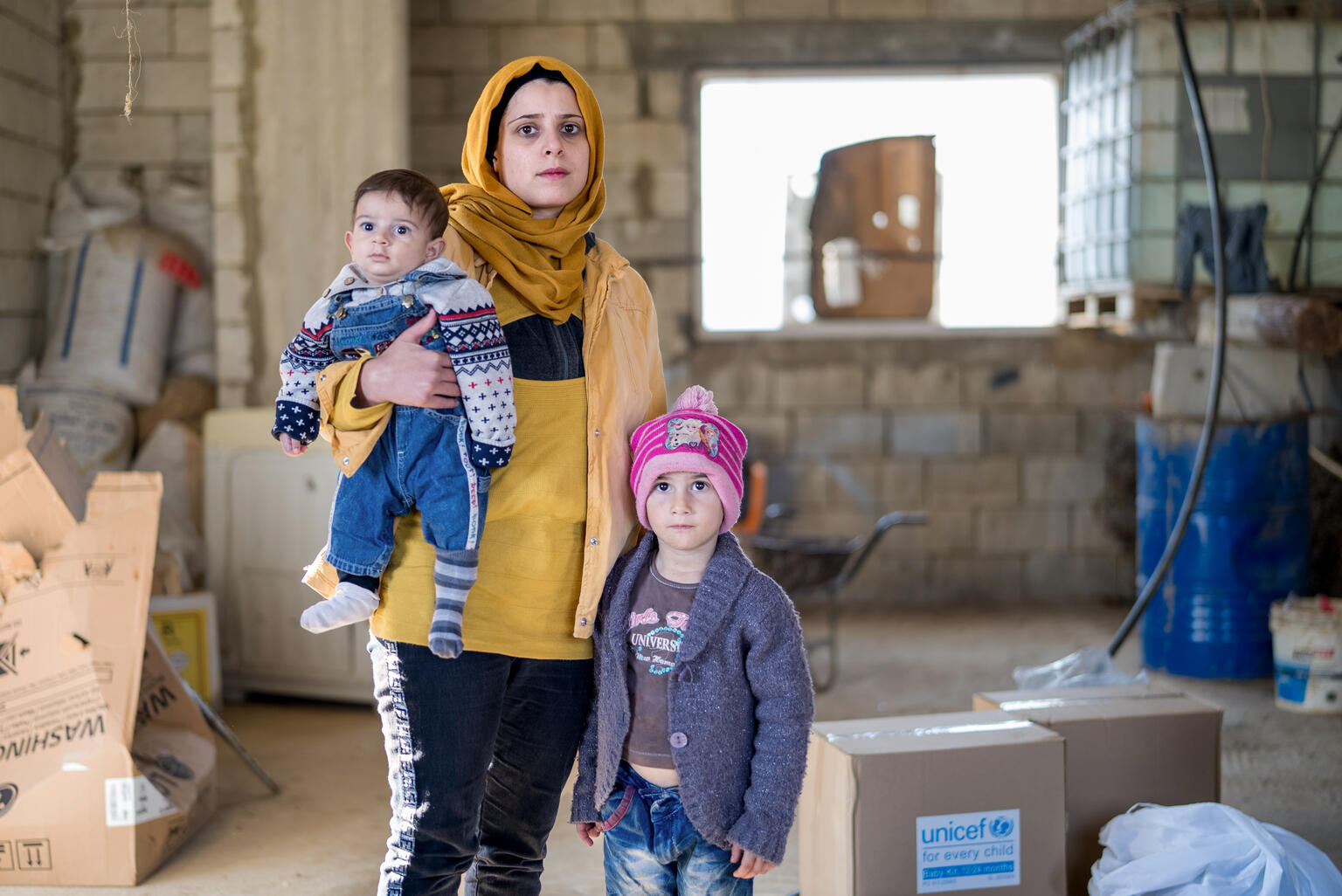 In Lebanon, a mother holds her baby while her older child stands beside her.