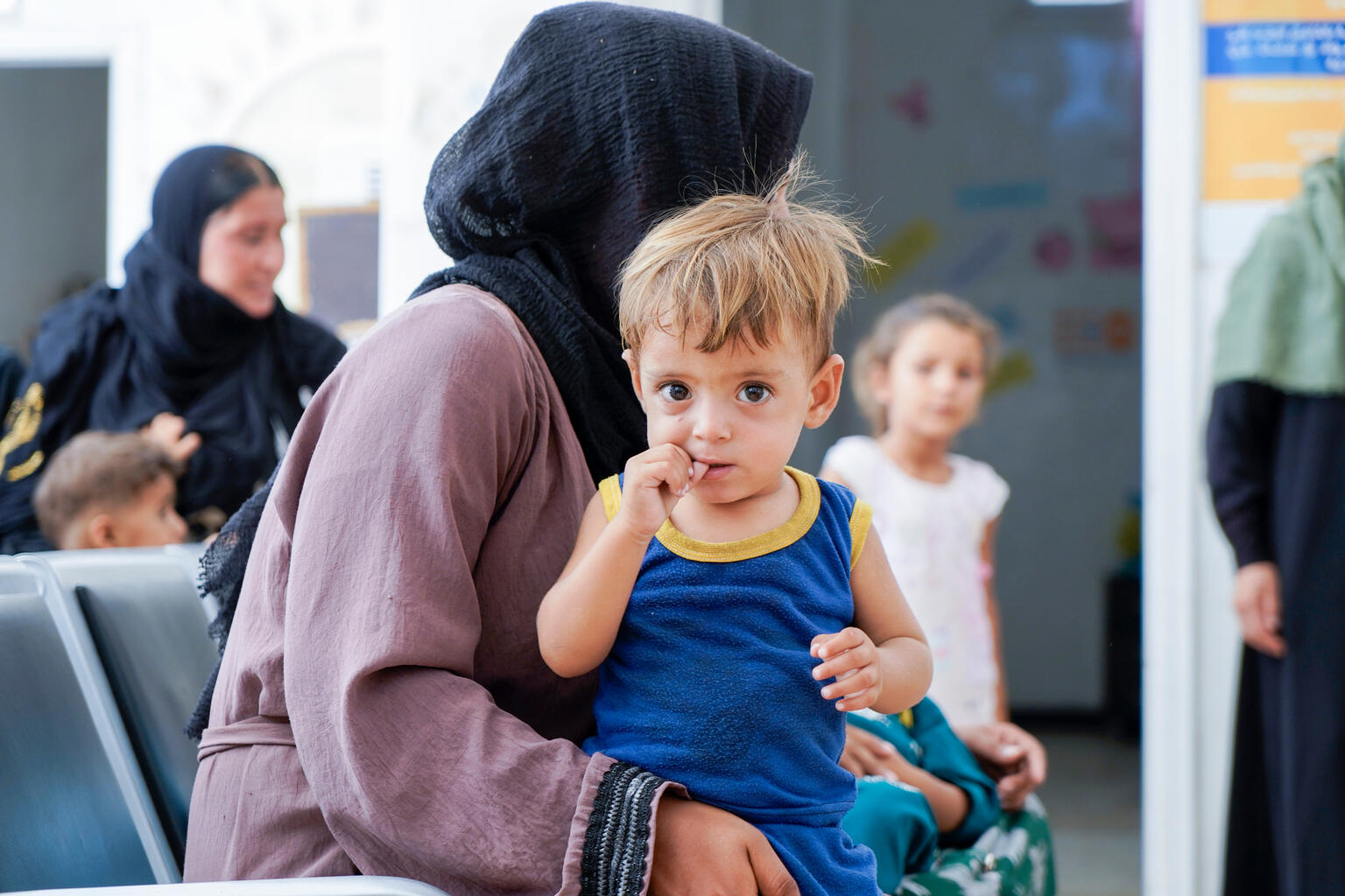 A child sitting on the lap of a woman wearing a black headscarf looks at the camera. 