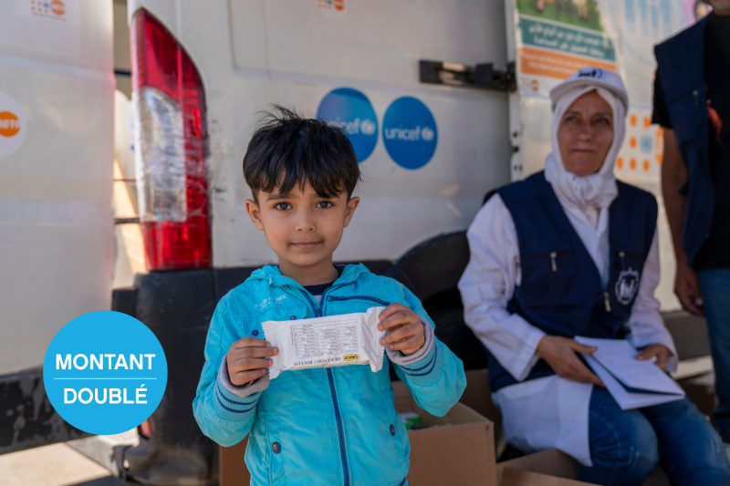 Un enfant à l’expression calme regarde l’objectif en tenant un sachet d’aliment thérapeutique dans un centre de l’UNICEF.