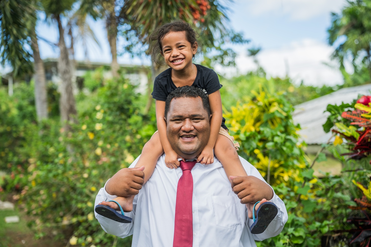 A father carries his daughter on his shoulders as they smile for a photo