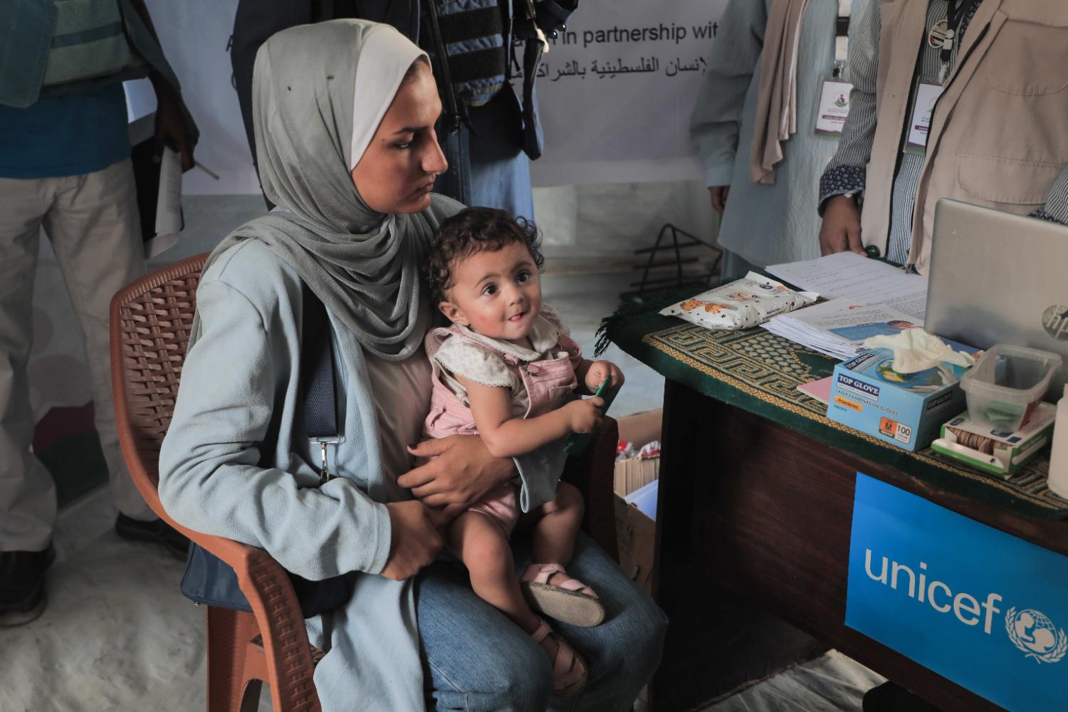 Une mère avec son bébé sur les genoux reçoit des produits alimentaires dans la ville de Gaza.