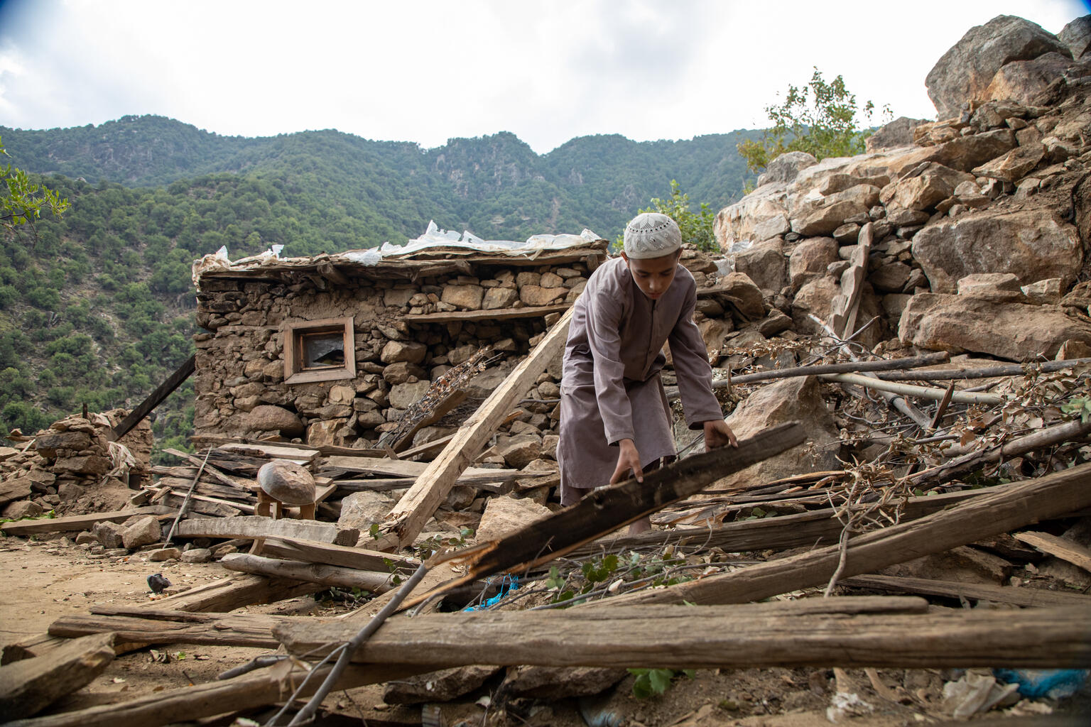 A boy clears wooden debris outside a damaged house in Afghanistan after an earthquake.