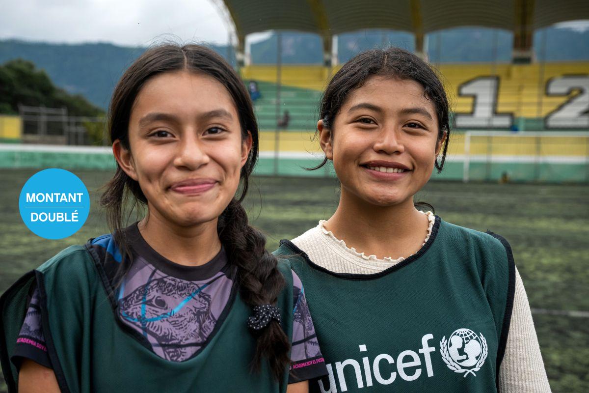 « Deux personnes souriantes portant des gilets verts UNICEF, debout sur un terrain de sport. »
