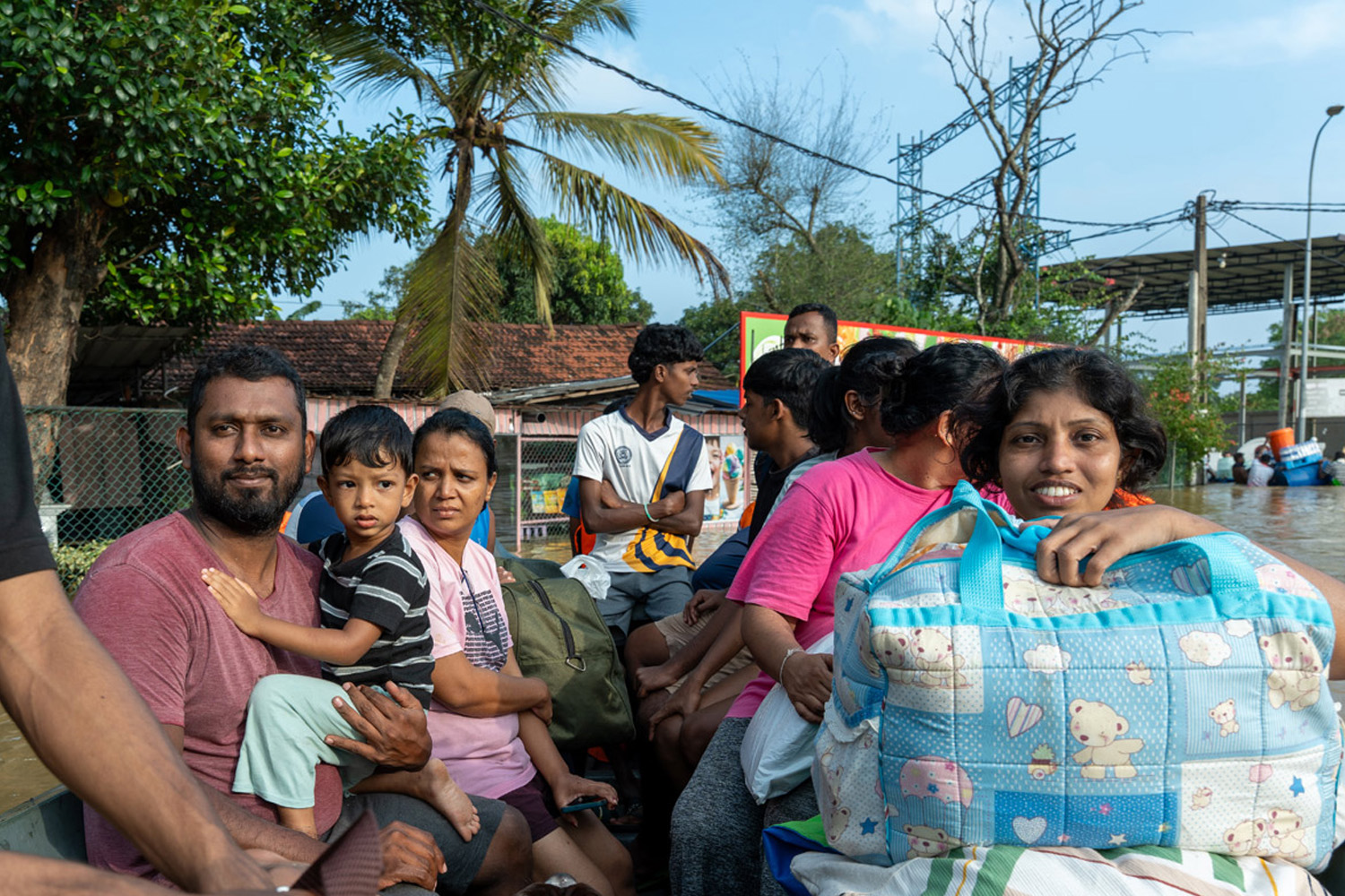A group of people (including a child) on a boat with their bags and belongings travel through a flooded street.