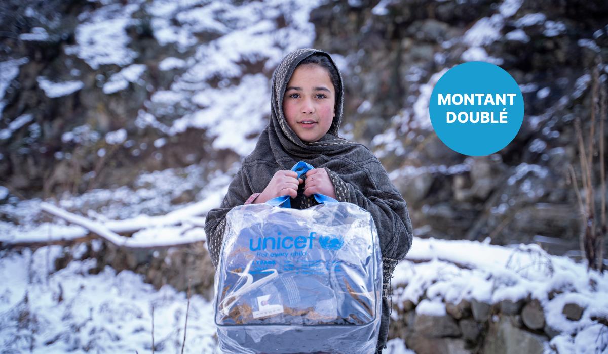 Une jeune fille dans la neige au Pakistan tient un sac à l’effigie de l’UNICEF contenant une couverture et des vêtements. 