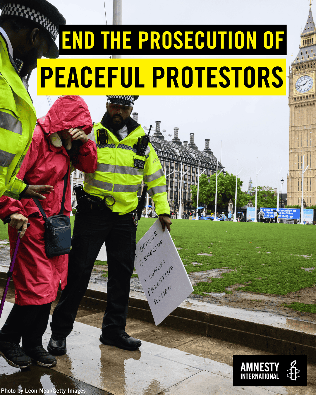 Two uniformed policemen escort a woman. She is wearing a long red coat with a hood covering her head.