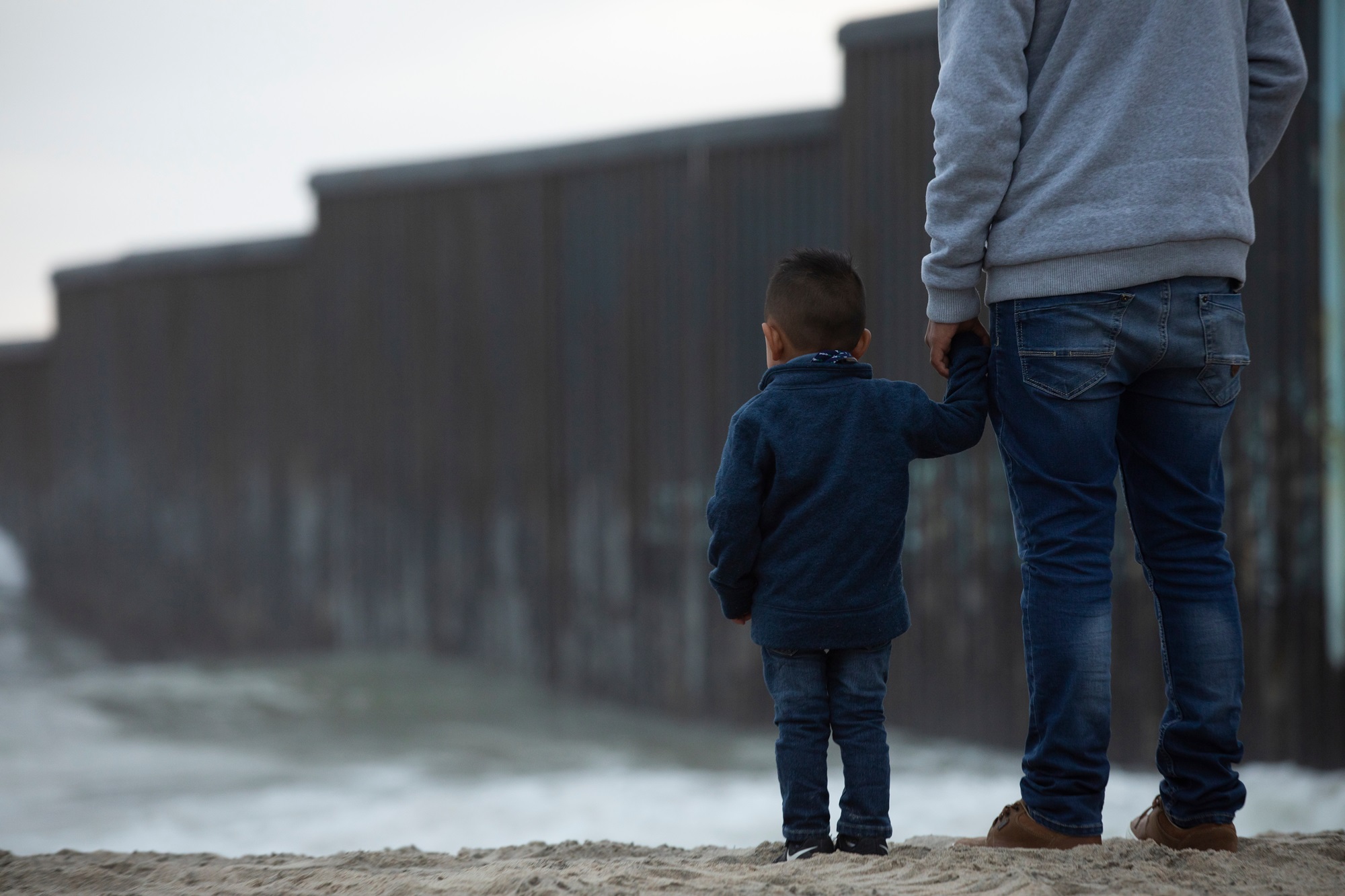 Tijuana, Baja California, Mexico - April 11, 2021: A father and son stand in front of the USA Mexico border wall.
