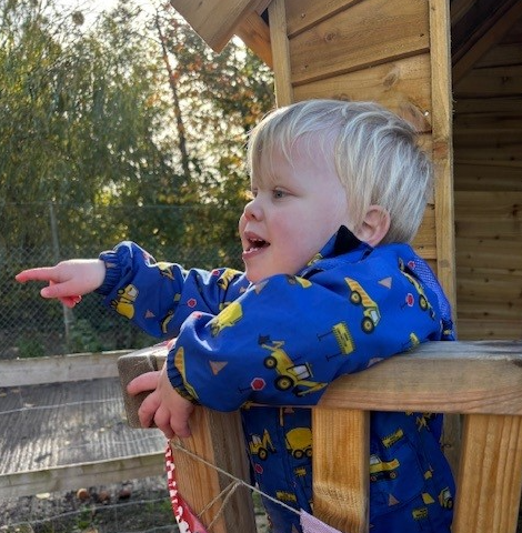 A young boy looks out from a playhouse smiling and pointing 