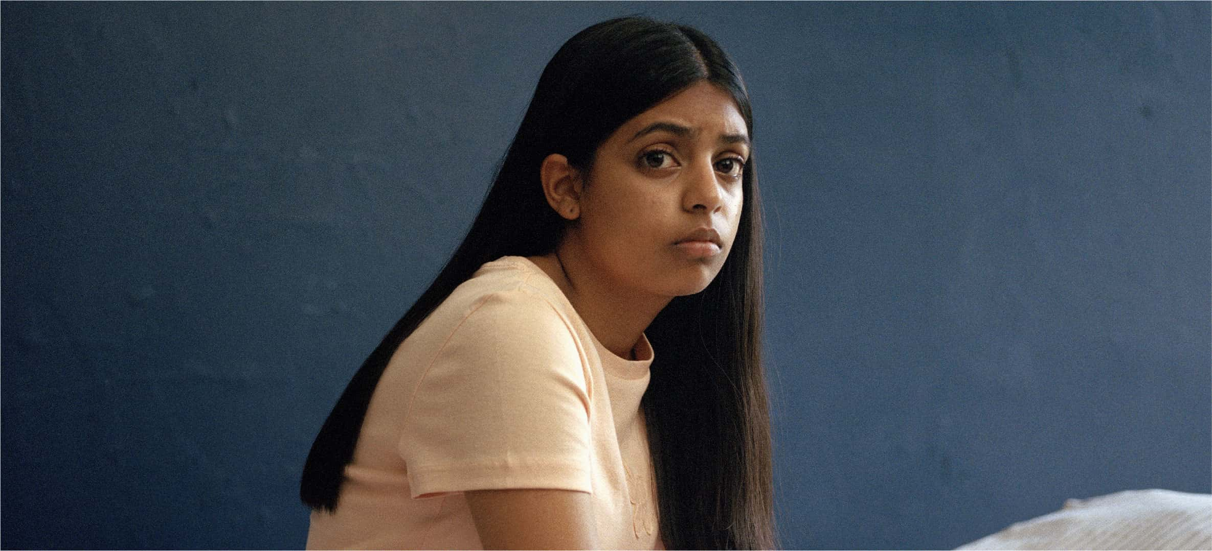 Young woman with long hair wearing a light-colored shirt, sitting against a blue background.