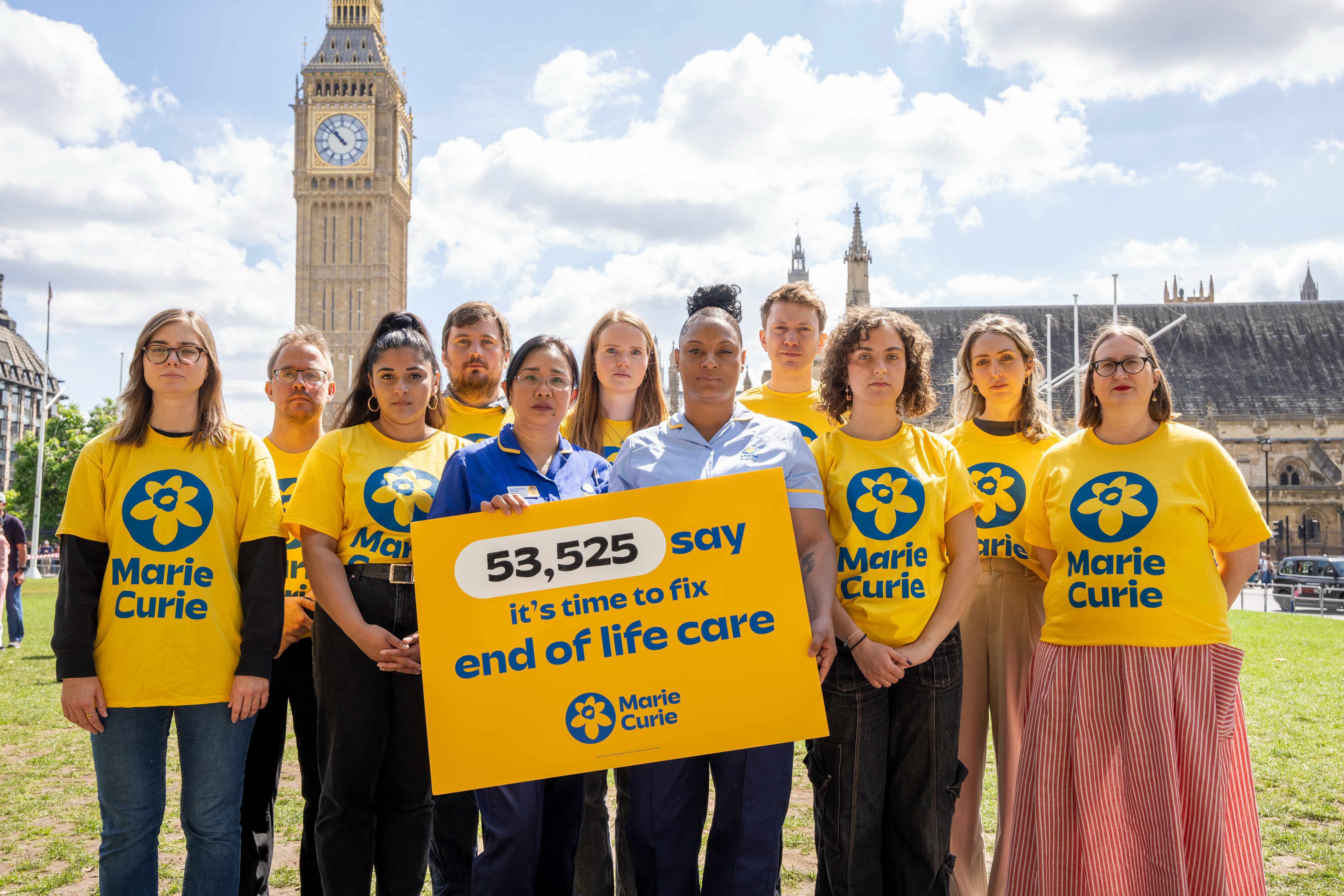 A group of people in yellow Marie Curie t-shirts holding up a campaign placard with Big Ben in the background