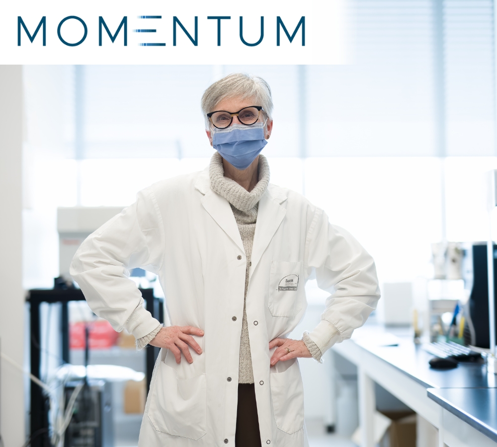 Dr. Christine Bear standing in her well-lit lab wearing a white jacket with her hands on her hips.