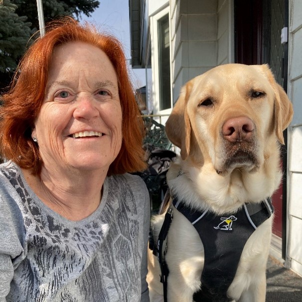 Alison Chilvers sitting outside smiling at the camera with her guide dog Weasley