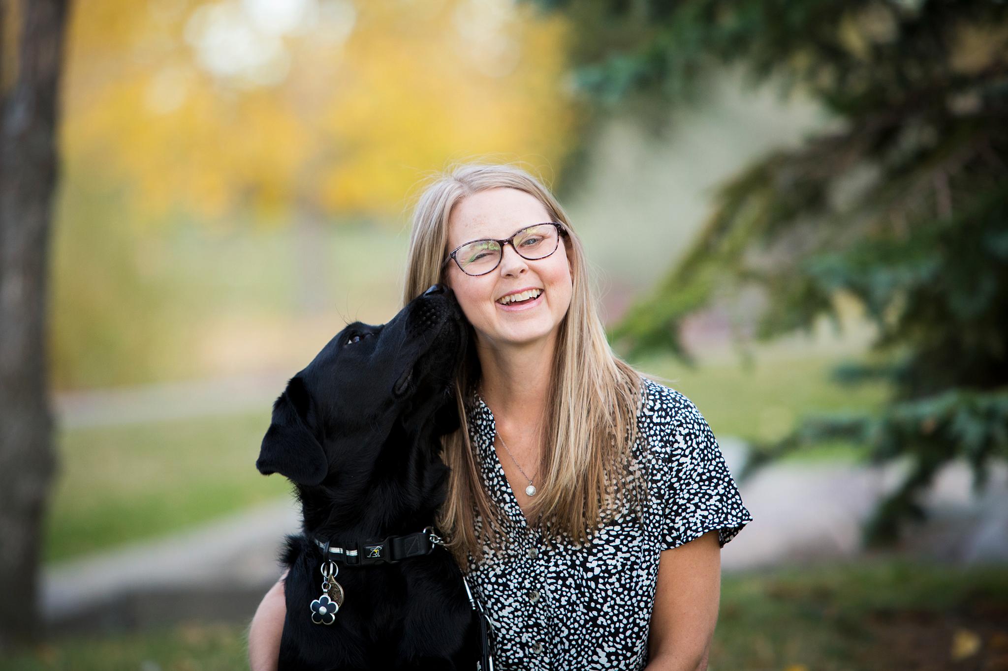 Becki is smiling next to her CNIB guide dog, Lulu who is sniffing her ear.