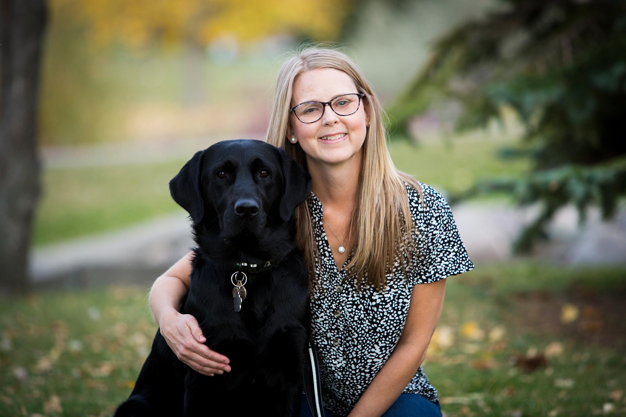 Becki smiling with her arm around her guide dog Lulu, a black Labrador