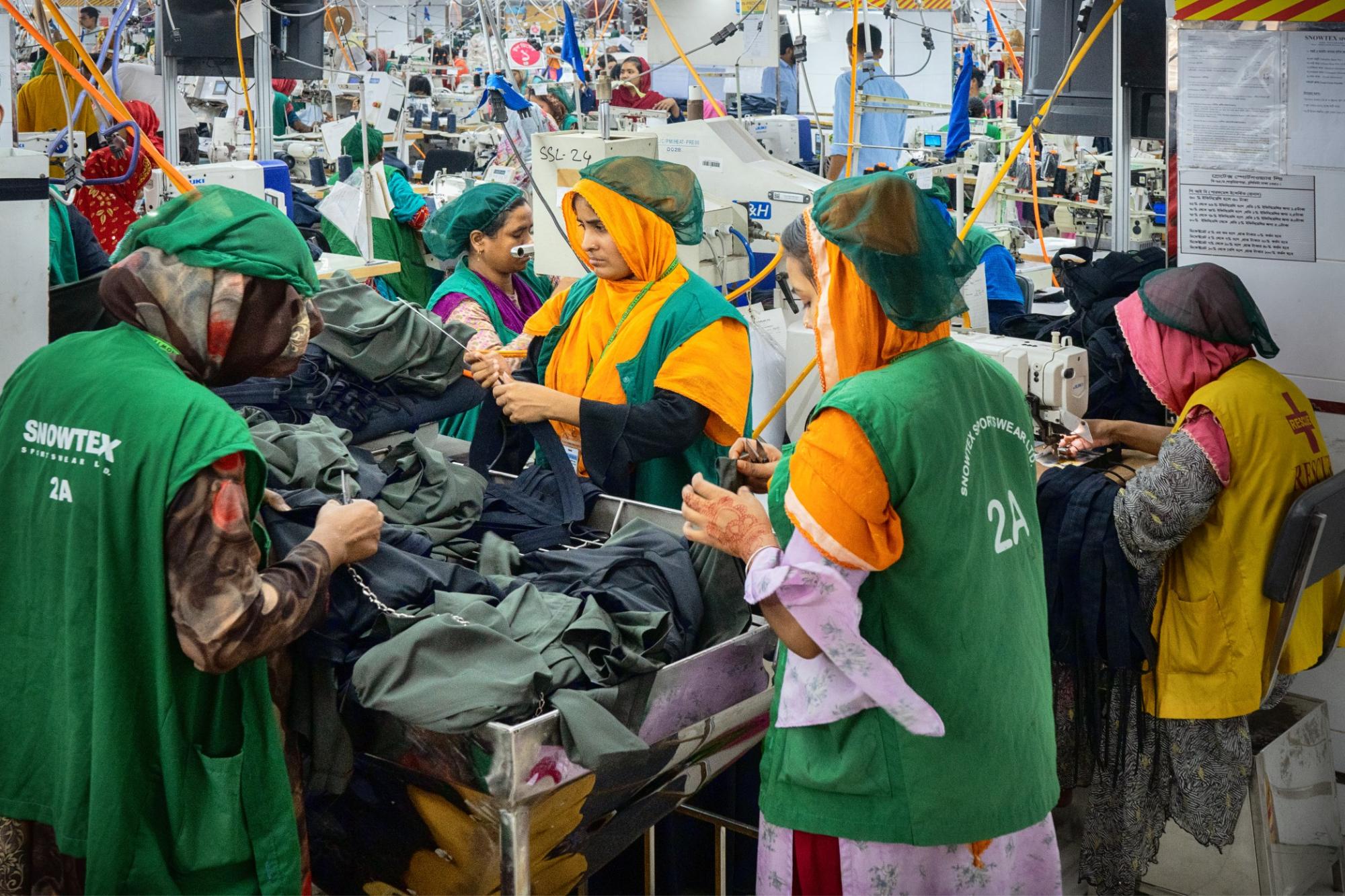 Women wearing green vests and hair-nets, working in a garment factory in Bangladesh.