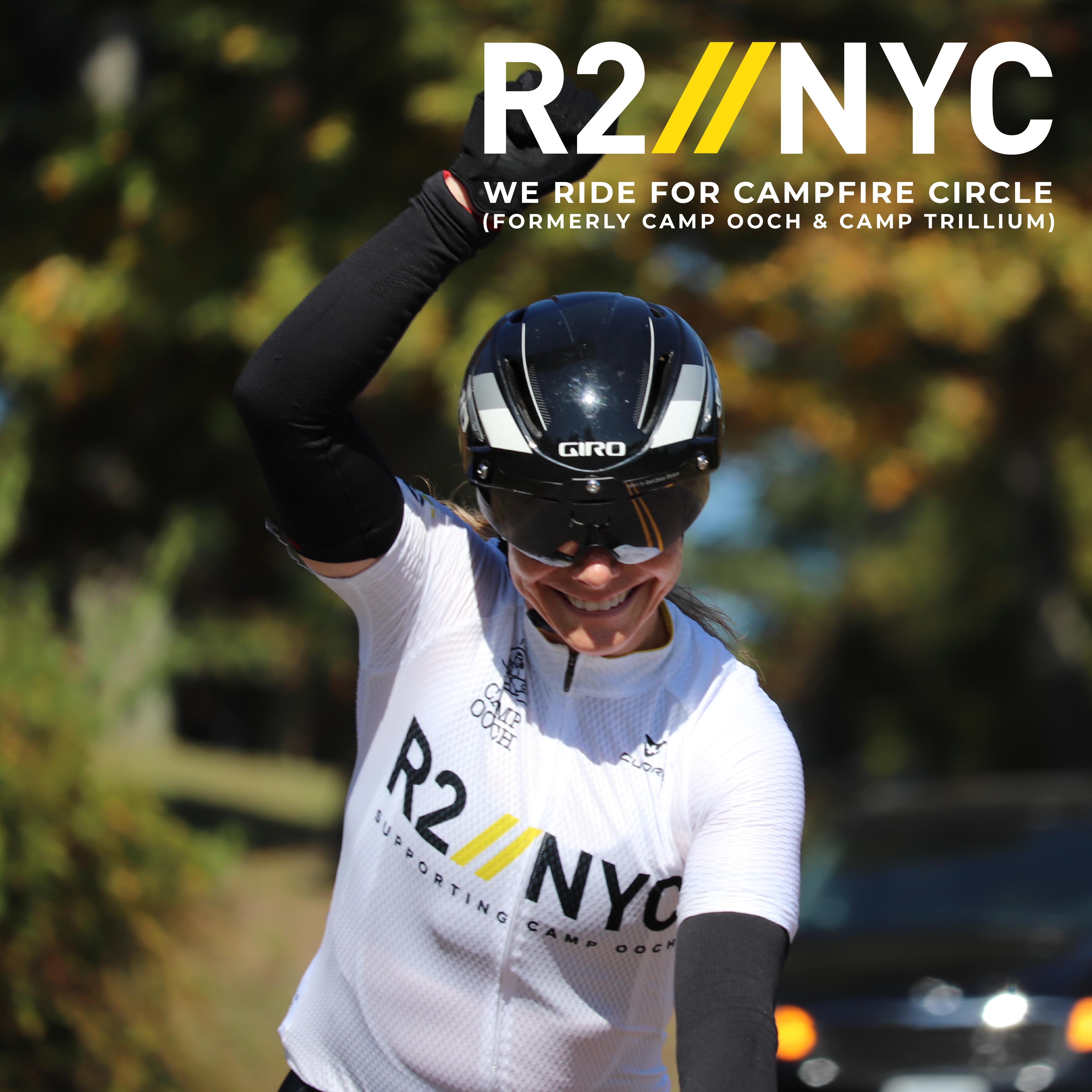 R2NYC We ride for Campfire Circle (Formerly Camp Ooch & Camp Trillium) Rider on bike, smiling with hand raised in the air and car and trees in background