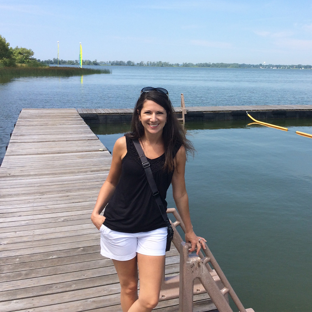 woman surrounded by water and trees, is standing outside on dock on the lake at camp in muskoka