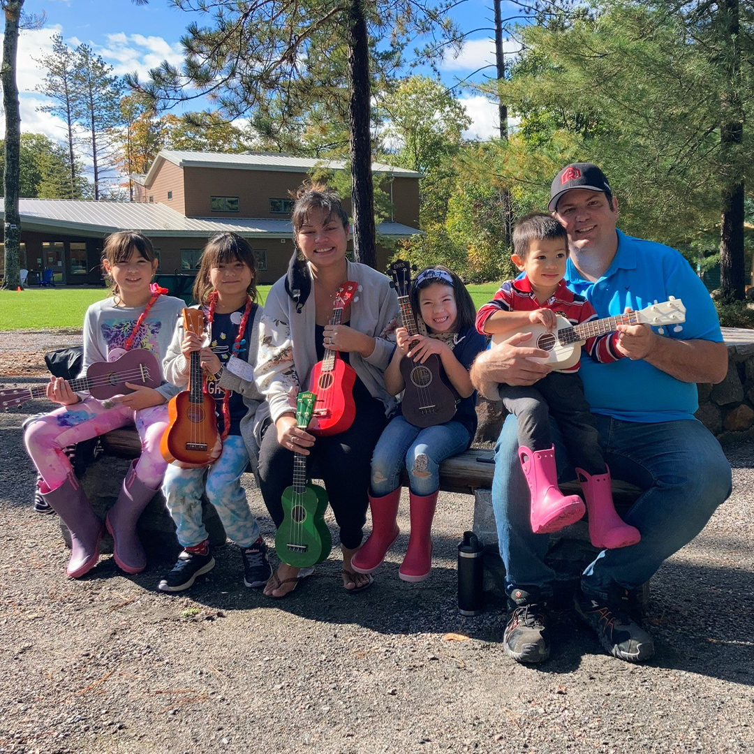 family sitting on picnic table outside holding ukuleles