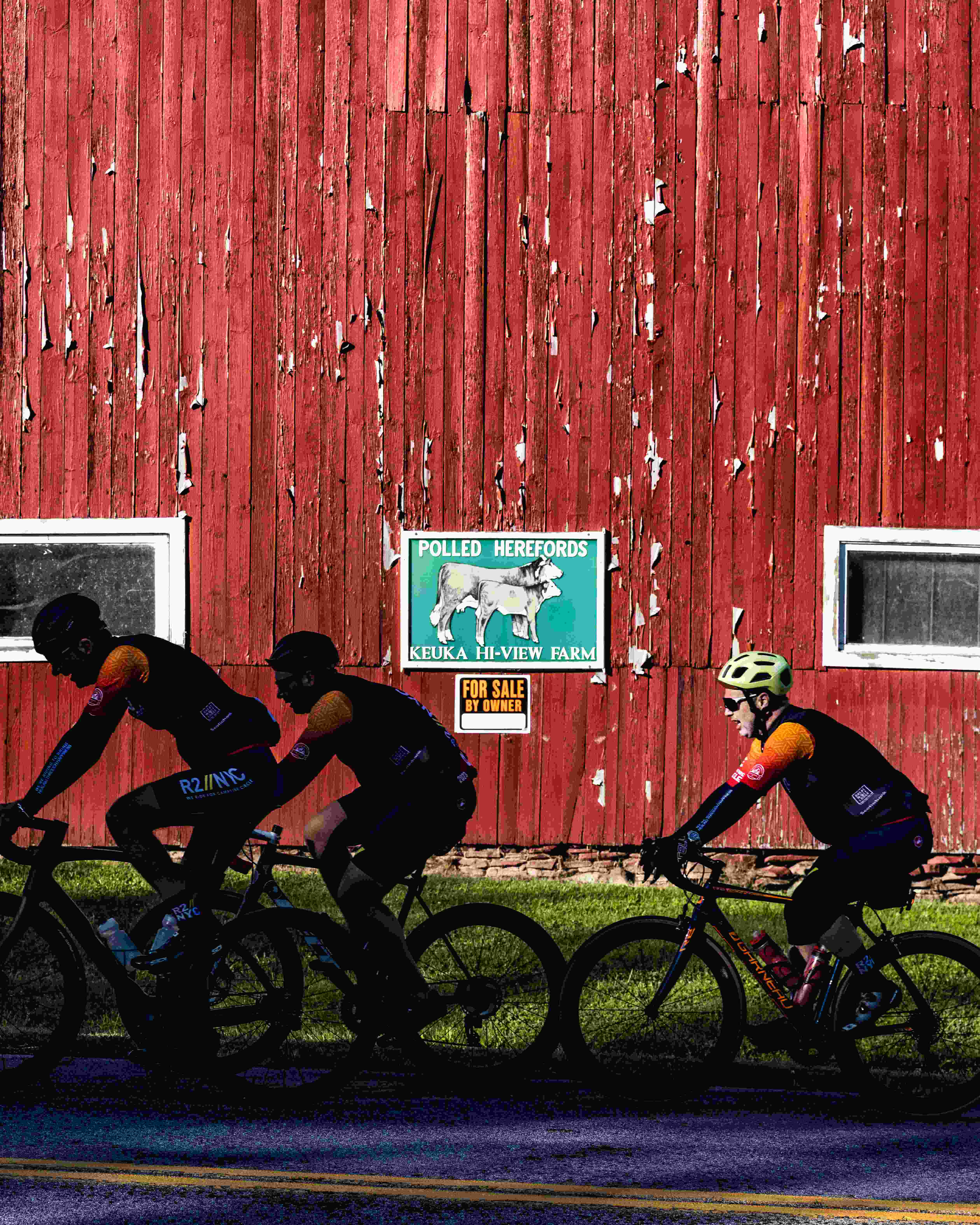 cyclists on the road, riding next to a worn down red barn