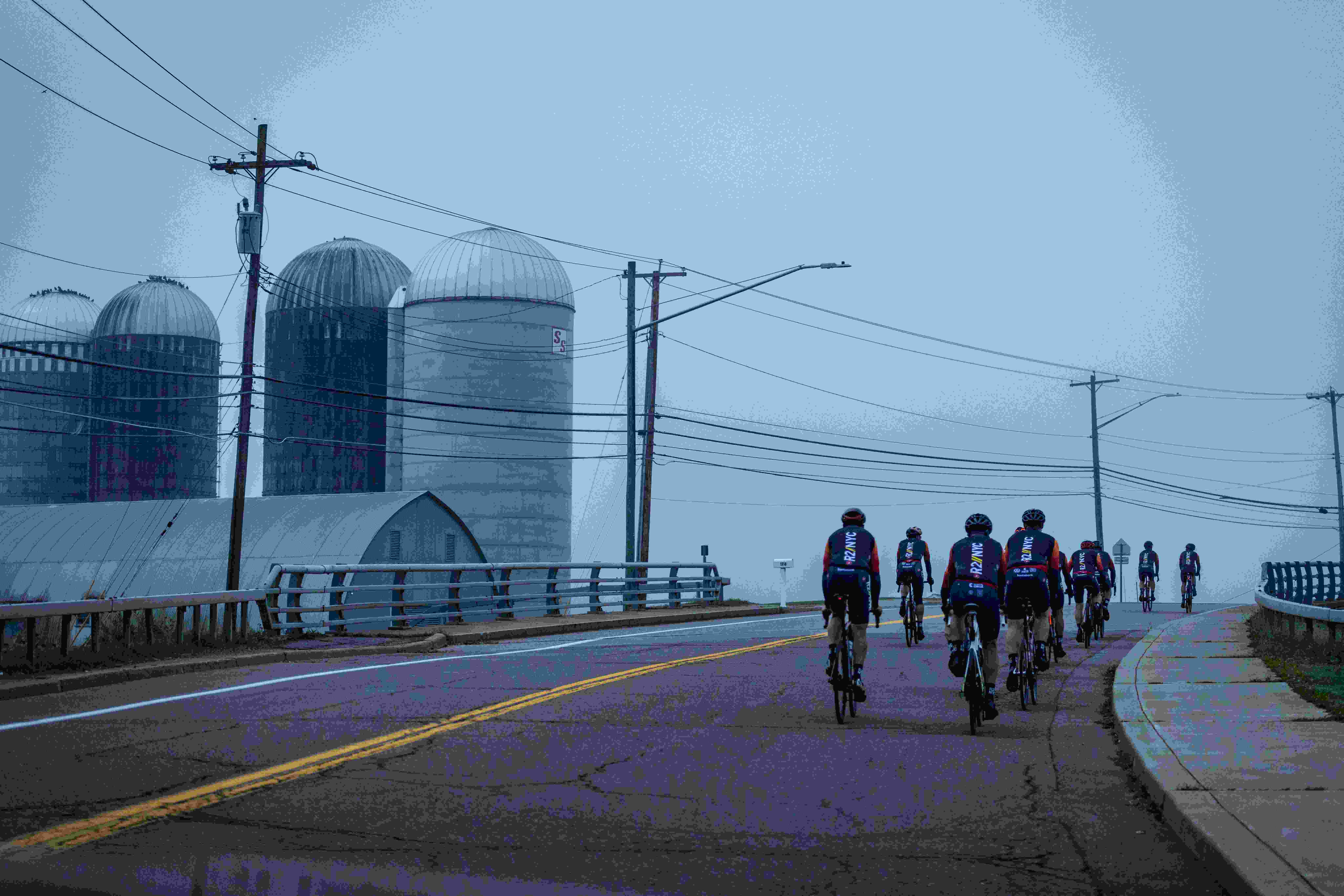 cyclists riding on a cloudy day with silos on the left