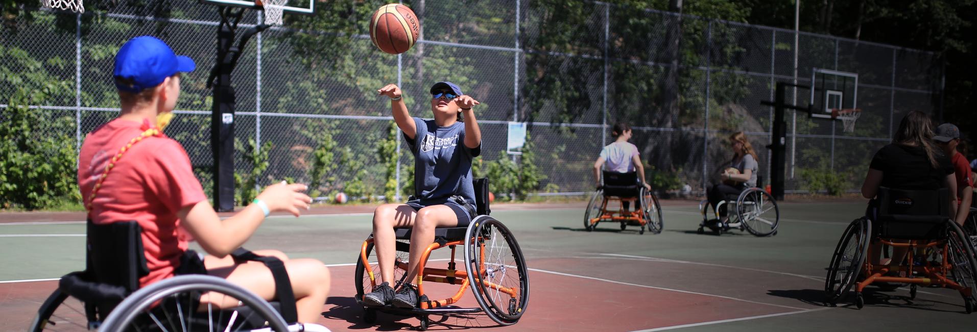 campers in wheelchairs playing basketball at camp