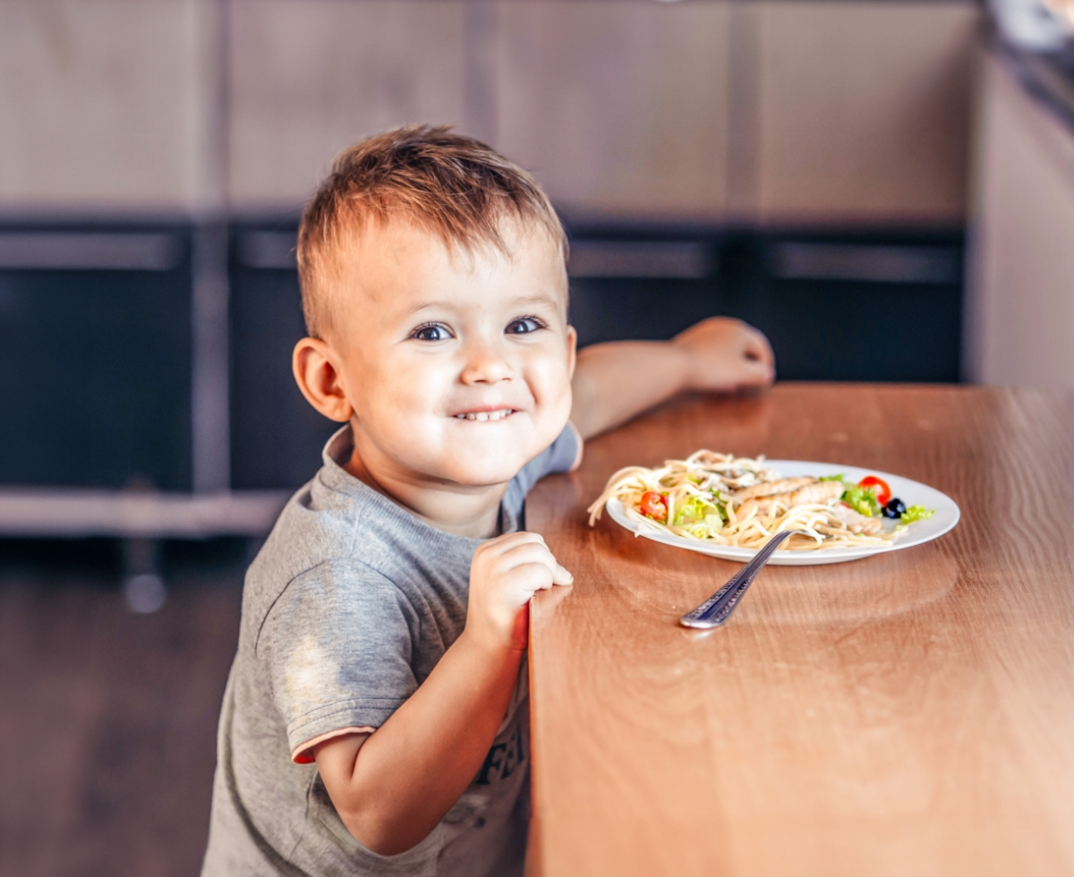 a child smiling with a plate of food infront