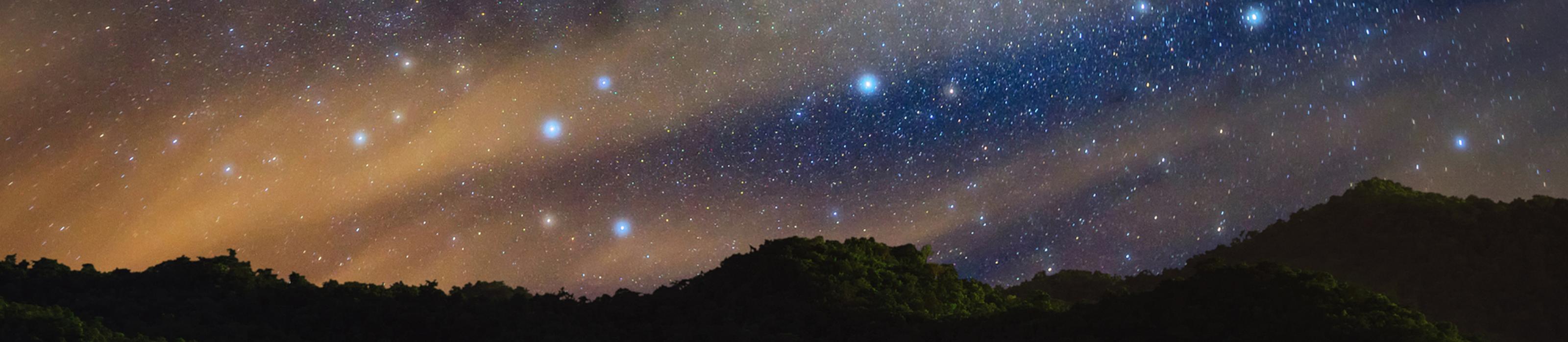 The Milky Way shines in the night sky above the silhouette of a mountain range. © standard Canva license