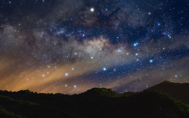The Milky Way shines in the night sky above the silhouette of a mountain range. © standard Canva license