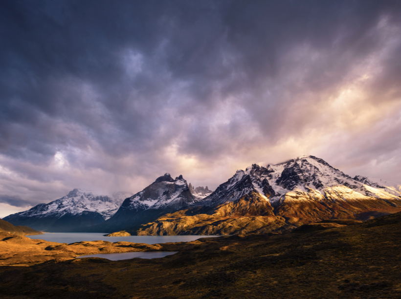 Alpine lake with three mountains in the background against a cloudy sky