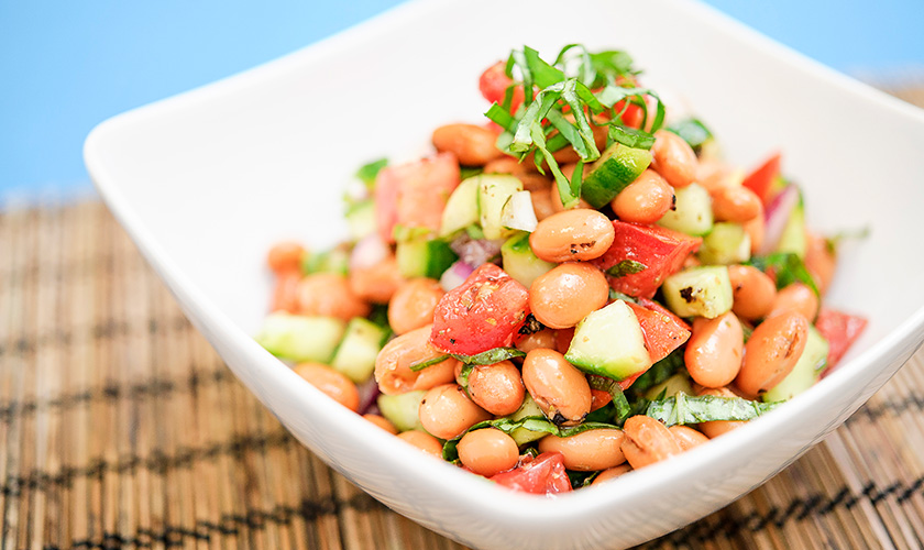 A bowl of Greek Bean Salad: beans with tomatoes, cucumber, red onion, and fresh herbs.