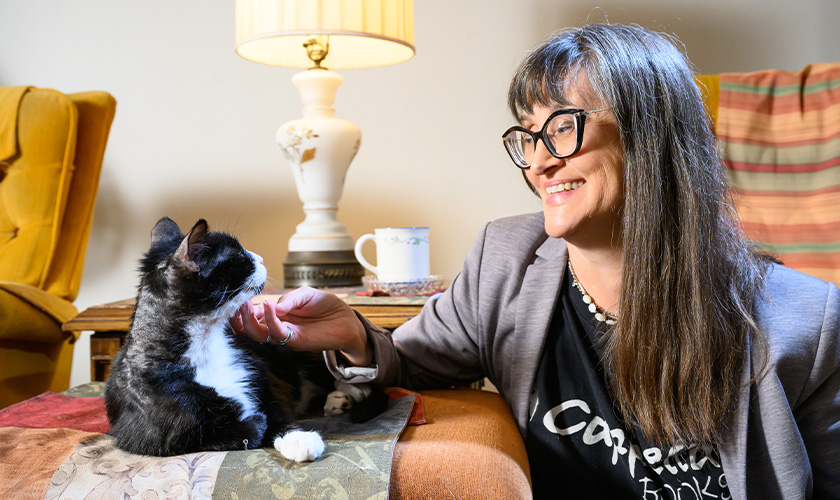 A woman [Jen] smiles while petting a tuxedo cat [Oscar] in a cozy home setting.