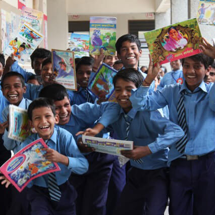 Photo of group of smiling school boys holding up books in a library
