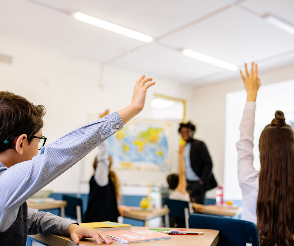 This is an image of children in a classroom with their hands up.