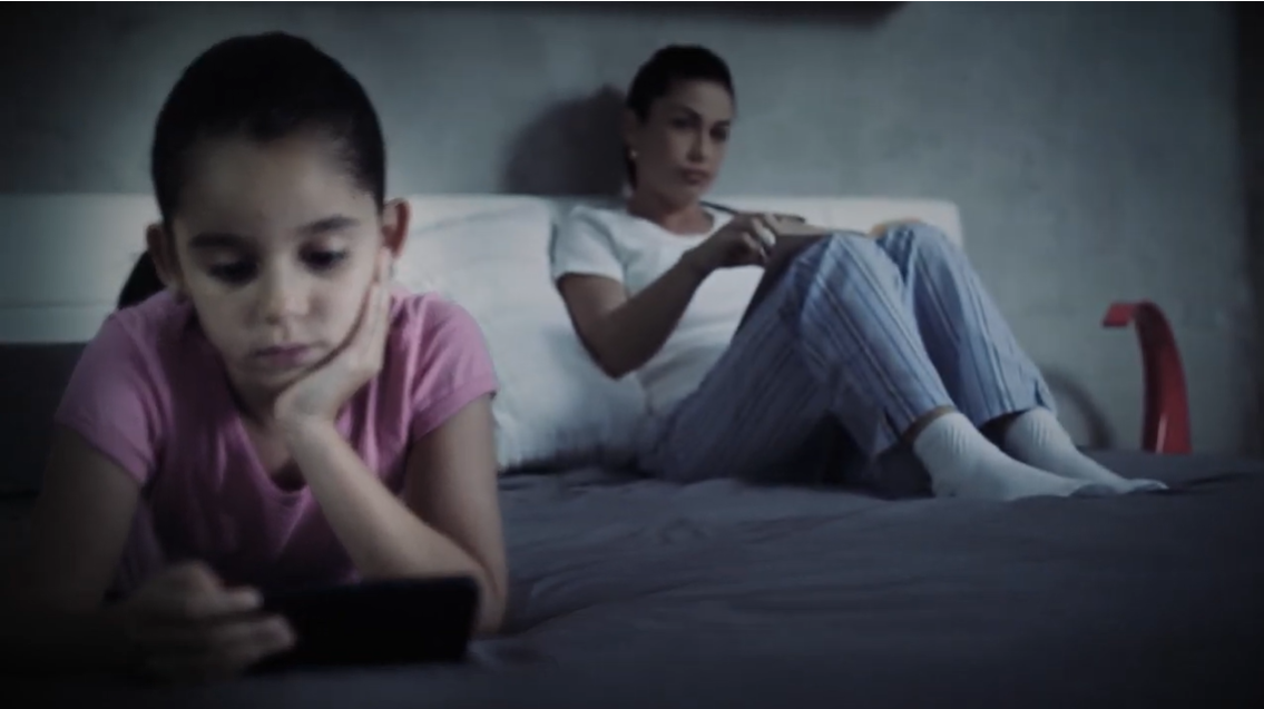 Screenshot from CCDH's PSA: girl looking at her phone while lying in bed with her Mum