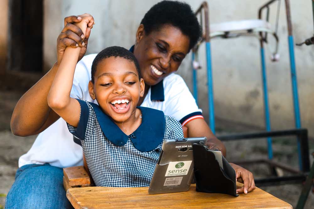 A girl smiles as she looks at a tablet branded Sense International 